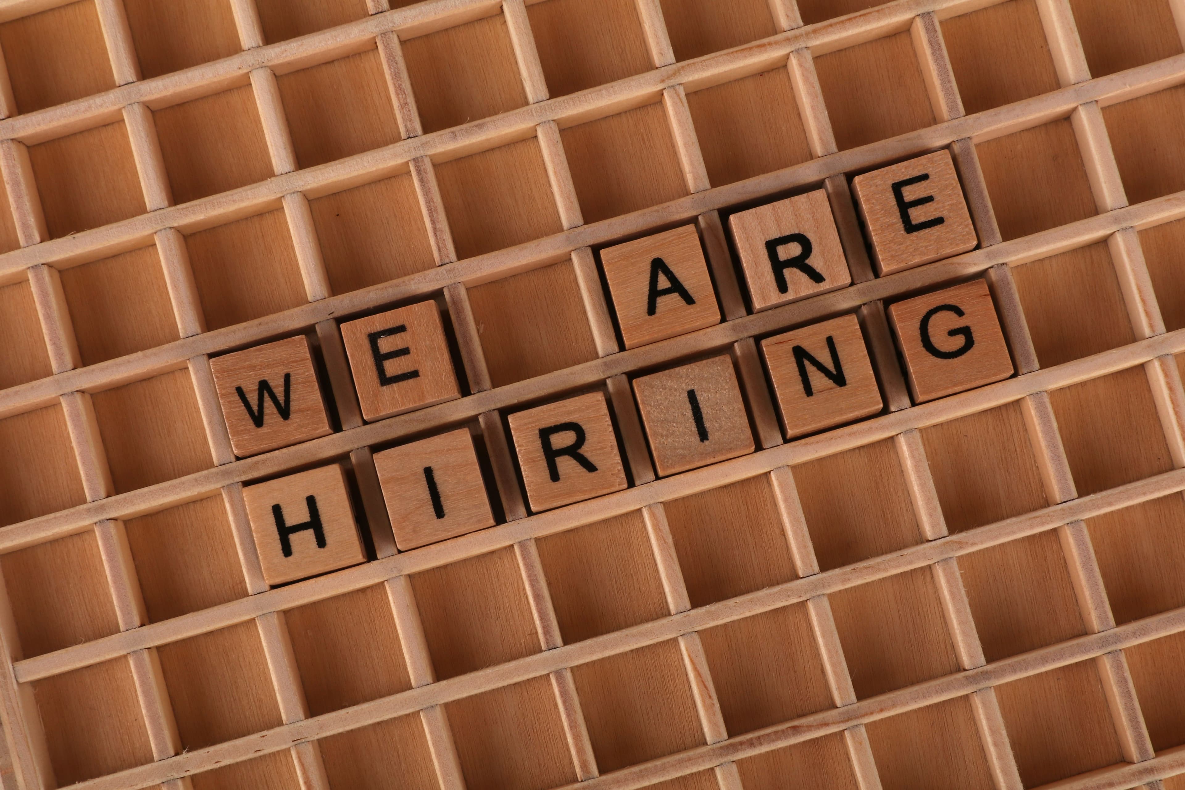 Wooden letter tiles arranged to spell We Are Hiring on a table